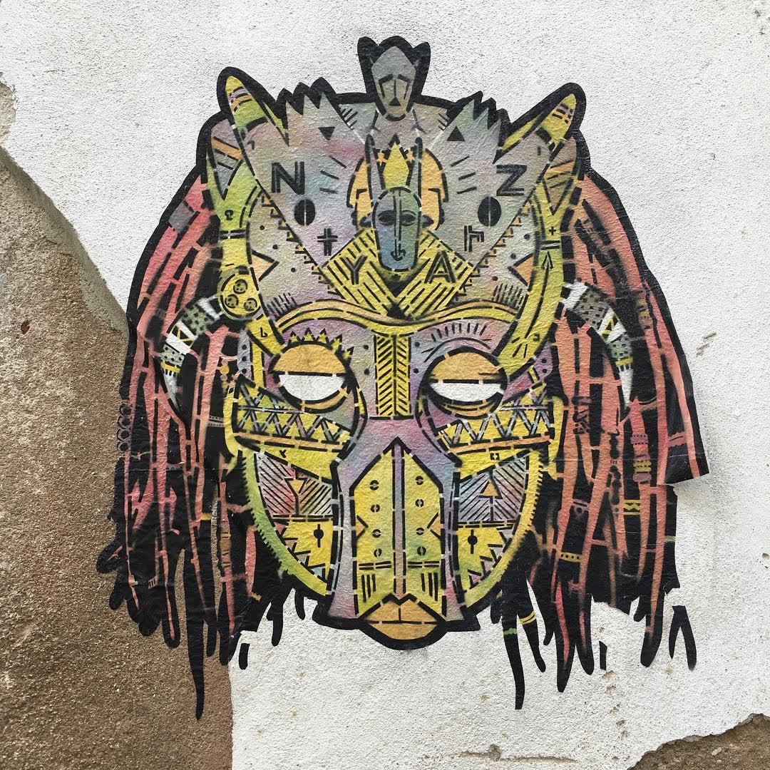 Street art in Lisbon: a tribal-style mask with long dreadlocks, pasted on a white wall