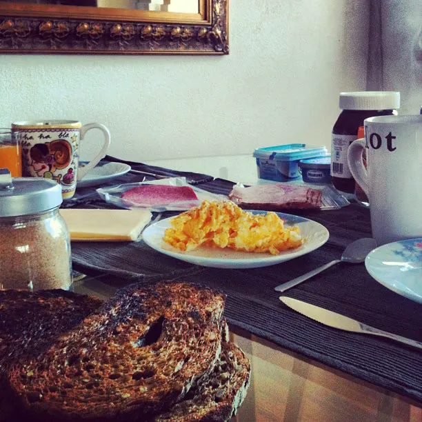 A breakfast table with scrambled eggs, toast, ham, cheese and mugs
