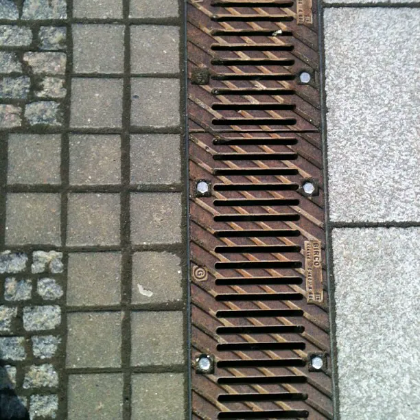 A long metal drain grate set in a stone pavement