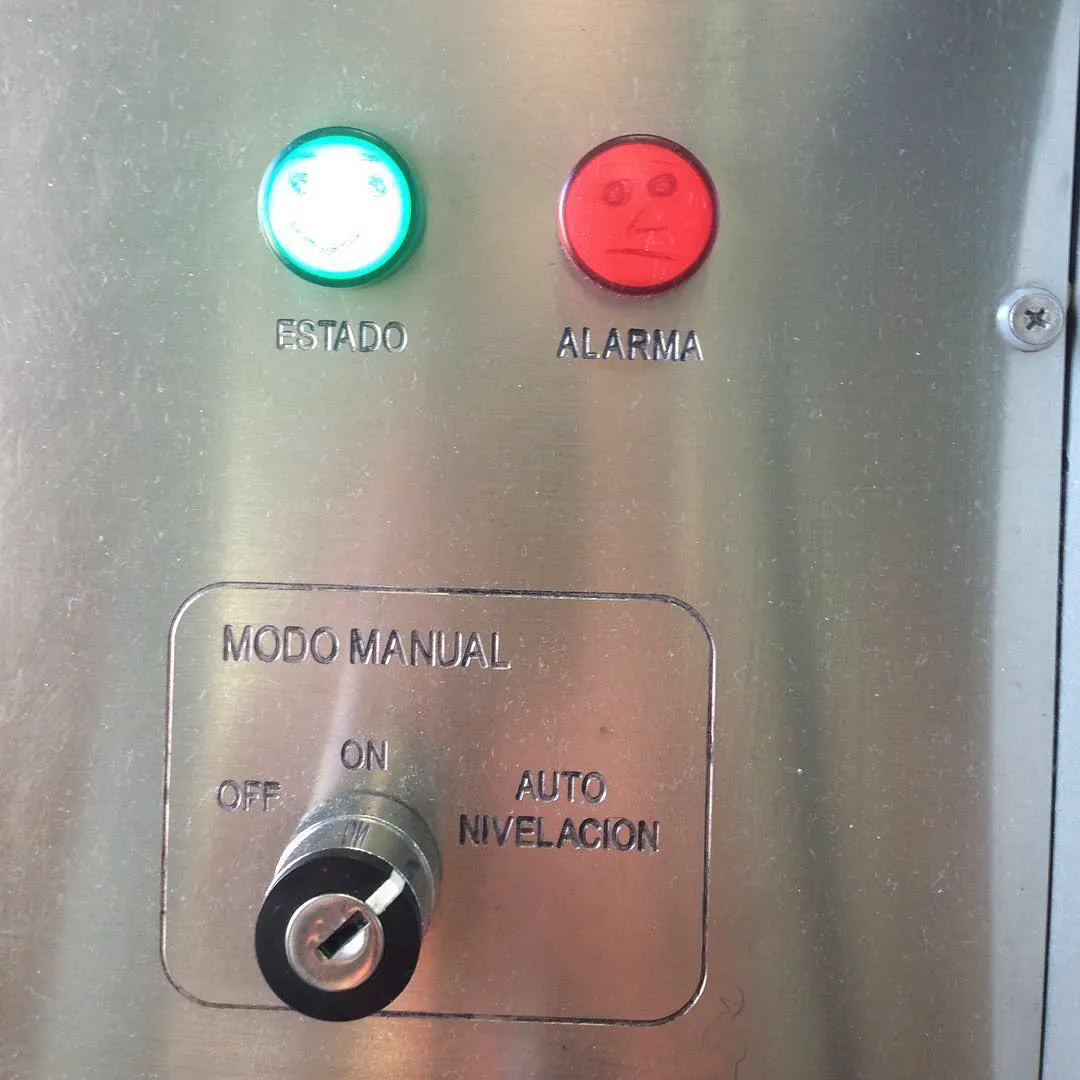 A steel control panel with a green 'Estado' light and a red 'Alarma' light, both drawn with smiling faces
