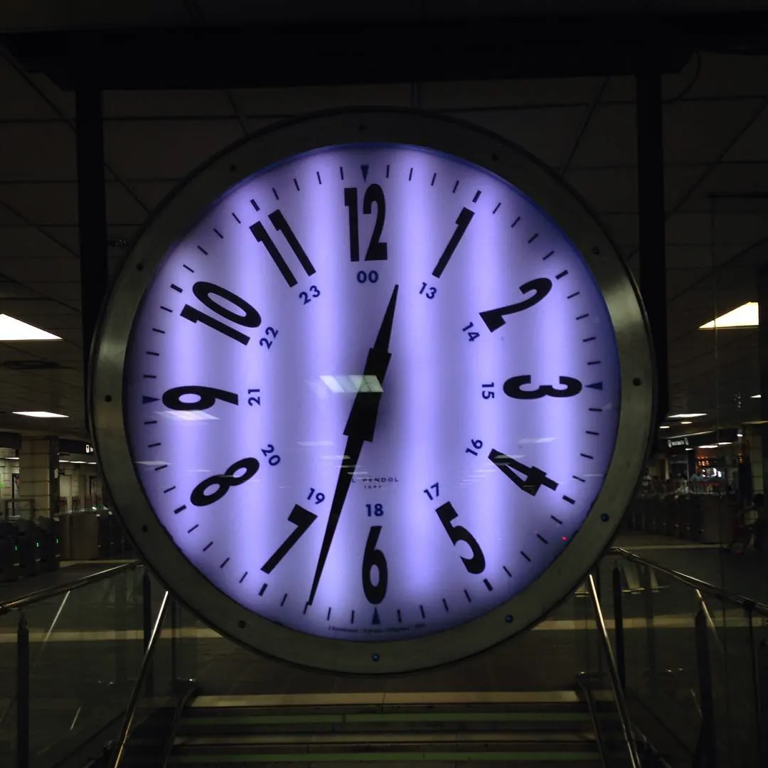 Un gran reloj de estación iluminado en violeta, en Plaça de Catalunya