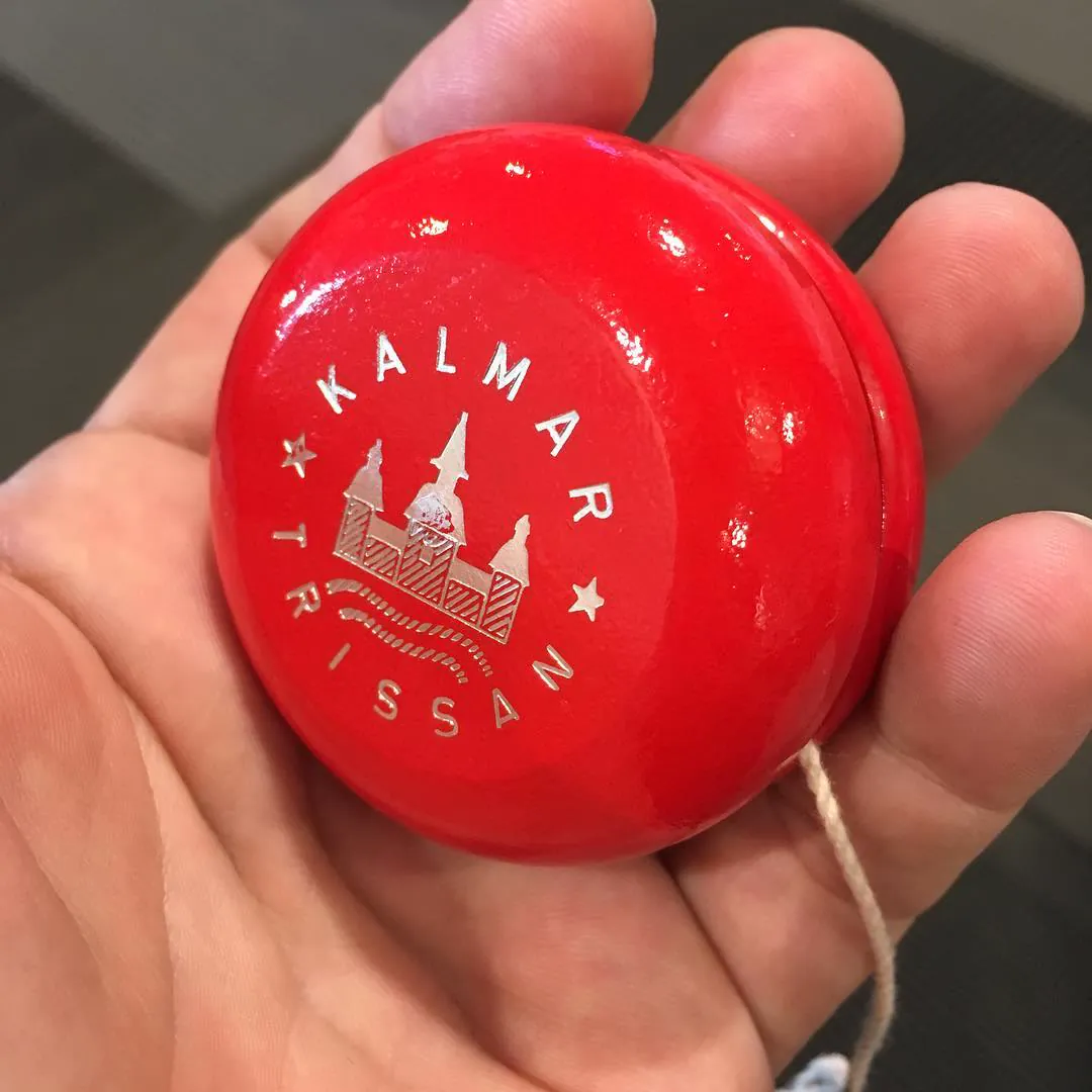 A hand holding a red wooden yo-yo printed with Kalmar