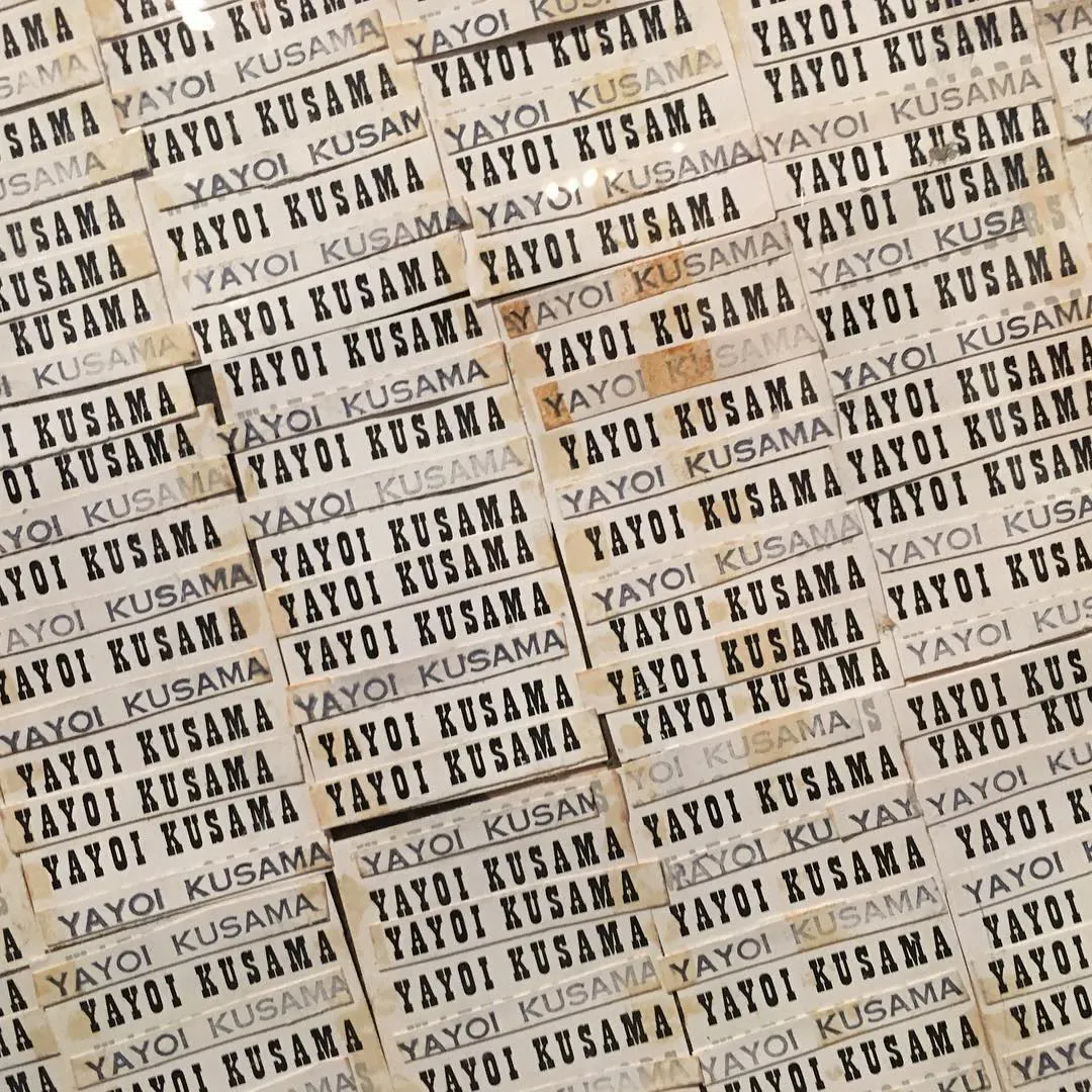 A wall covered with labels repeating the name Yayoi Kusama