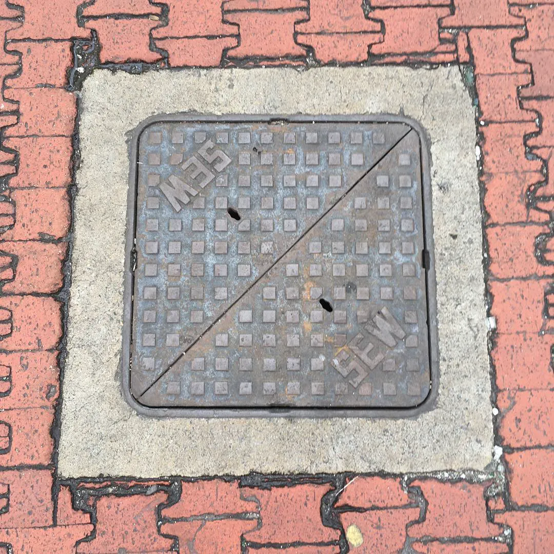 A square manhole cover stamped SEW, set in red brick paving