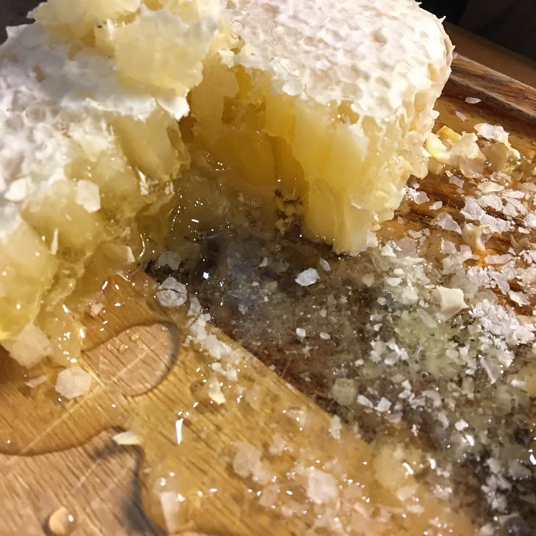 A honeycomb dripping raw honey onto a wooden board