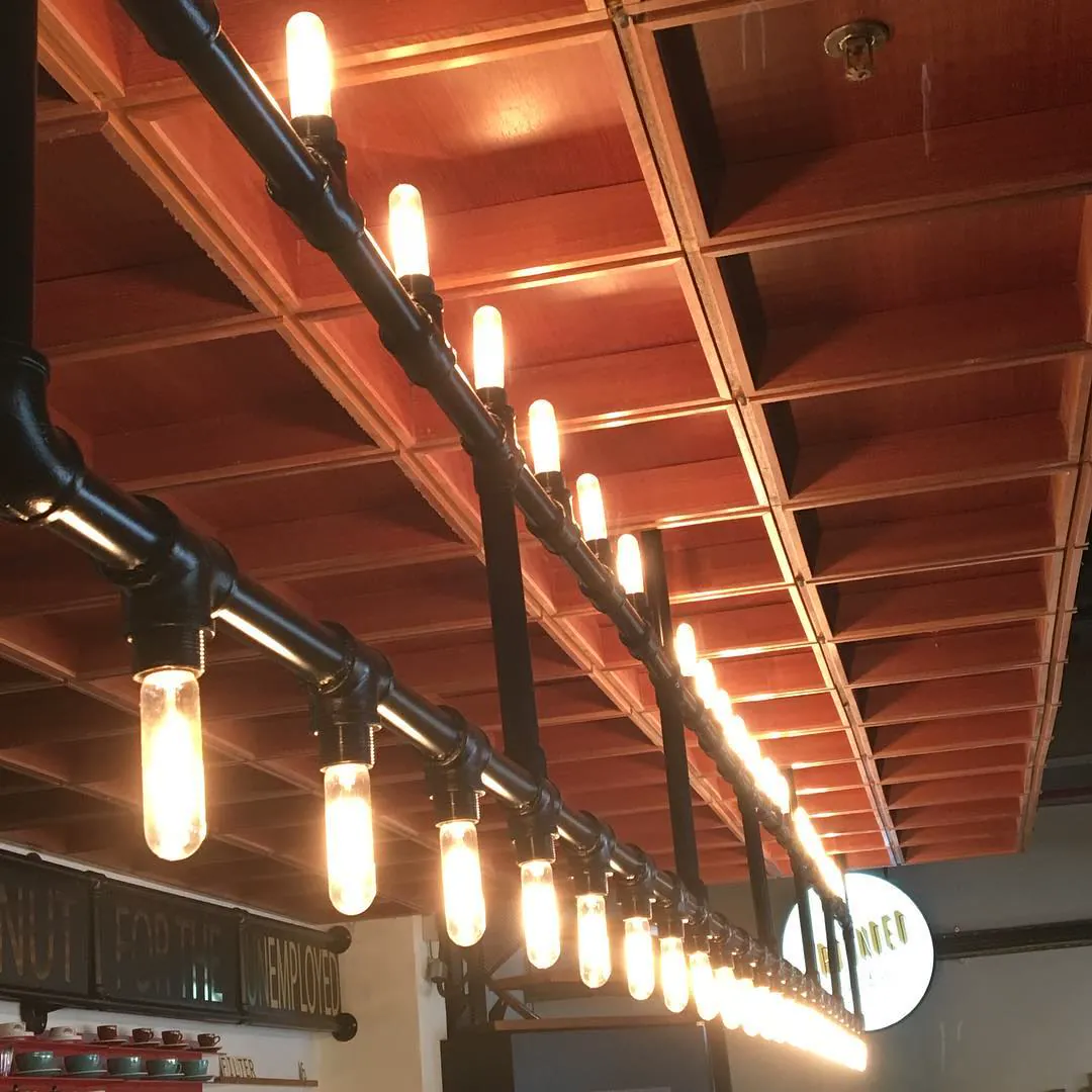 A row of bare light bulbs hanging from black pipes under a wooden ceiling
